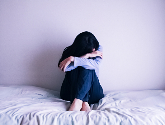 ベッドの上でうずくまって落ち込んでいる女性
