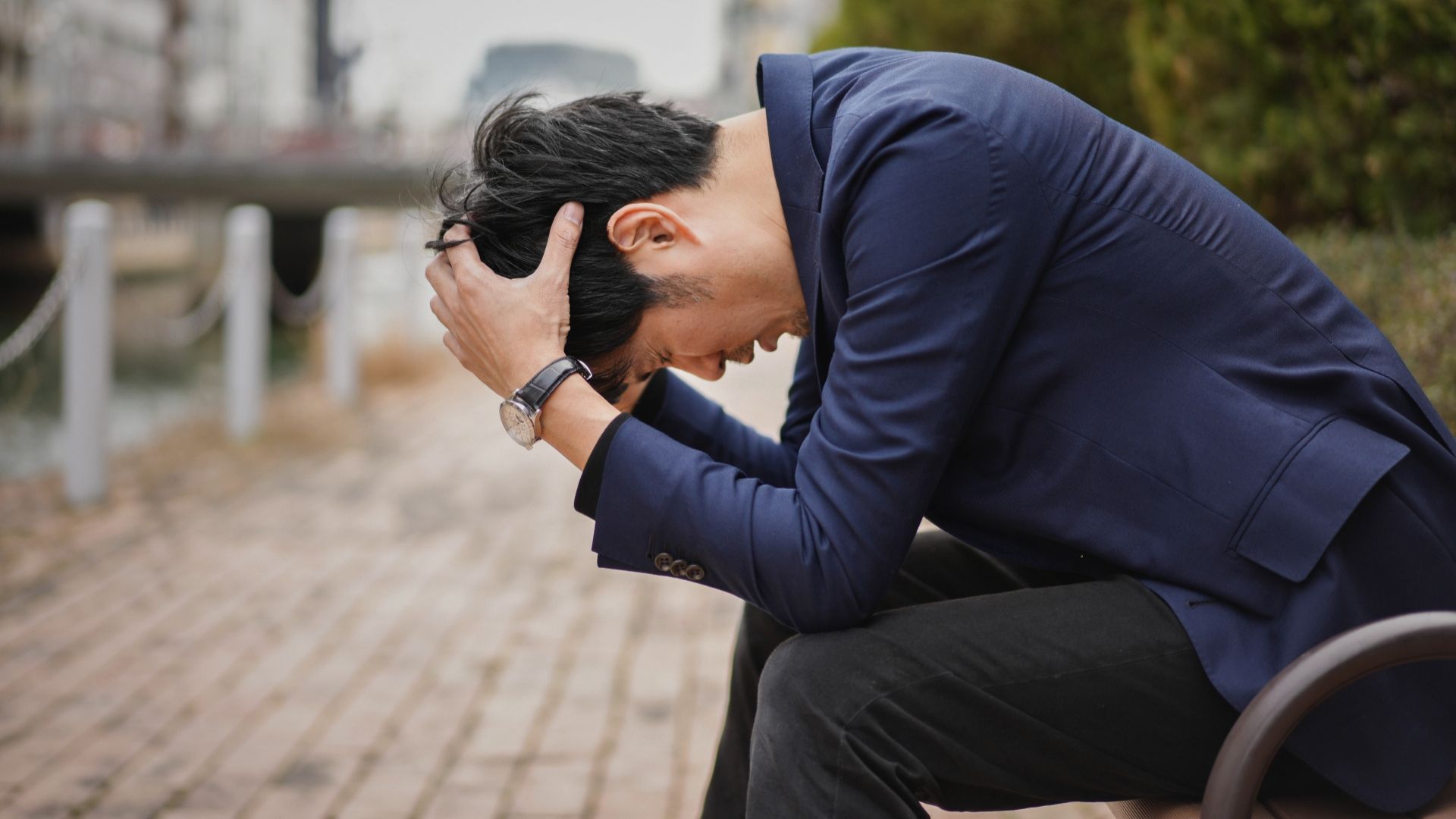 一人ベンチで座り頭を抱えて落ち込む男性
